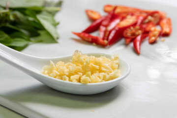 Chopped garlic in a spoon with red hot chili peppers and sweet basil leaves.