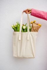 Holding eco handbag full of flowers on white background, close-up Canvas bag with blank space