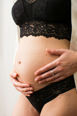 Closepu belly of pregnant young woman in black underwear with hands white background