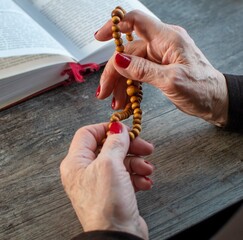 Close-up of an elderly woman's hands holding a rosary. Selective focus, the text is blurred.