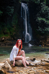 Beautiful girl with red hair enjoying life and beautiful nature. Behind the Abhesi Waterfall, Stones in the mountain river, Kutaisi, Georgia