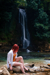 Beautiful girl with red hair enjoying life and beautiful nature. Behind the Abhesi Waterfall, Stones in the mountain river, Kutaisi, Georgia