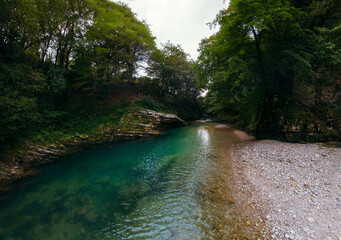 Obraz premium The Abhesi waterfall among green trees, a mountain river with clear water. the stones are turned by the stream. Tourist place for rest and swimming. Aerial view. western Georgia