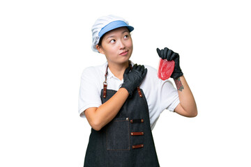 Young caucasian woman wearing an apron and serving fresh cut meat over isolated background looking up while smiling