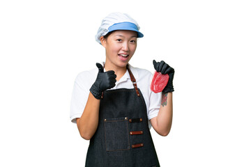 Young caucasian woman wearing an apron and serving fresh cut meat over isolated background with thumbs up because something good has happened