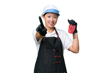 Young caucasian woman wearing an apron and serving fresh cut meat over isolated background showing and lifting a finger