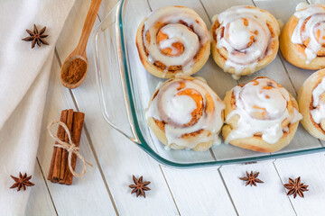 Delicious cinnamon buns covered with cream in a transparent baking tray on the table