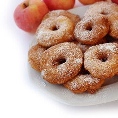 Homemade deep fried apple rings with batter sprinkled with powdered sugar on a plate isolated on white with fresh apples