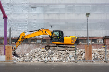 yellow excavator on a pile of construction debris on a construction site in front of a building...