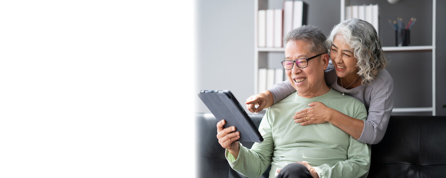 Happy Asian mature couple using a digital tablet in living room, spending time and bonding with each other.