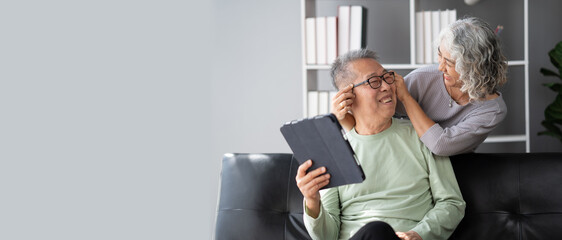 Happy Asian mature couple using a digital tablet in living room, spending time and bonding with each other.