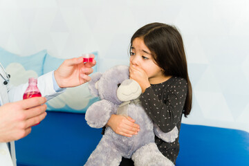 Pediatrician giving cough syrup medicine to sad kid patient