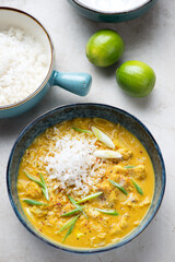 Bowl of yellow curry with fish and rice, studio shot on a light-beige stone background, elevated view