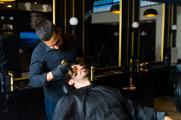 Fototapeta na wymiar Professional barber using a clipper machine with a client