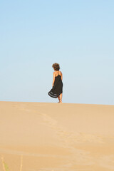 Anonymous woman in black dress on beach. Back view at distance of woman in black dress walking on spacious sandy coast