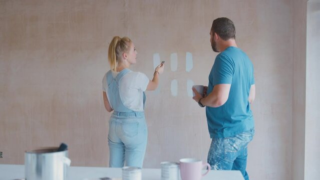 Couple renovating kitchen at home painting tester paint colour strips on plaster wall - shot in slow motion