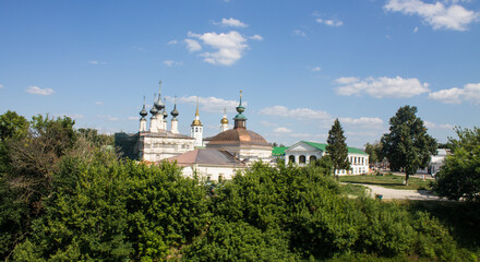 Fototapeta na wymiar A beautiful urban landscape - a panoramic view of historical architecture with temples among green trees with lush foliage on a sunny summer day in Suzdal, Vladimir region and a space for copy