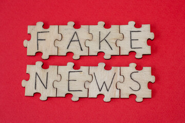 Wooden puzzles with Fake News on a red background. Misinformation, propaganda, clickbait, media...