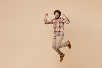 Fototapeta na wymiar Full body overjoyed happy fun young Indian man wear brown shirt casual clothes jump high do winner gesture clench fist isolated on plain pastel light beige background studio. People lifestyle concept.
