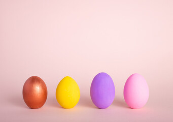 A row of colorful Easter eggs painted in simple colors on a light purple background - side view with copy space.