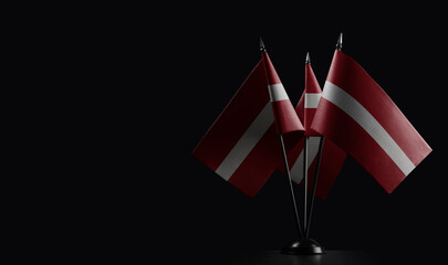 Small national flags of the Latvia on a black background - obrazy, fototapety, plakaty