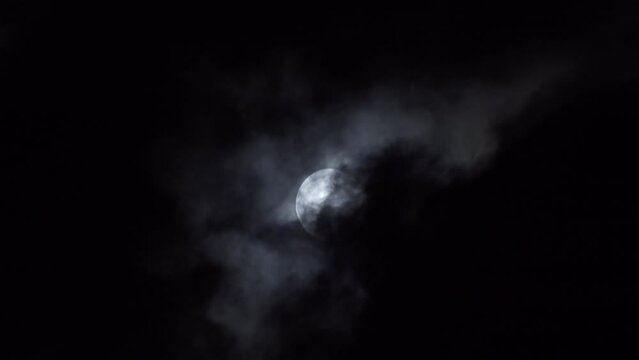 Black clouds float smoothly across the full moon at night. Dramatic Halloween concept in nature. black and white tone.