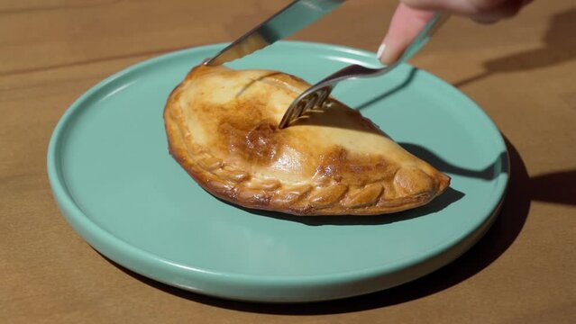 Female hands cuts a fresh empanada in half for breakfast. Close-up in slow motion with fork and knife