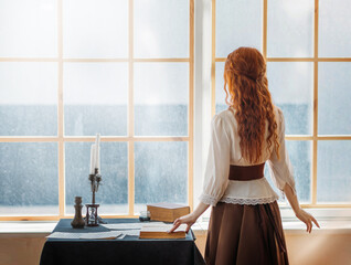 mysterious redhead woman stands in room near window waiting for love. Girl writer looking for...
