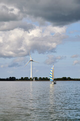 Segelboot vor einer Windkraftanlage bei wolkigem Himmel