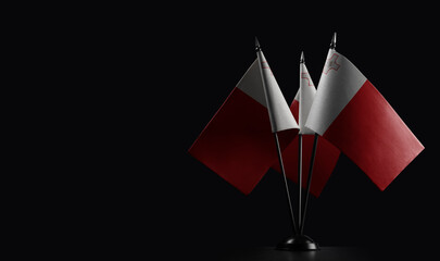 Small national flags of the Malta on a black background