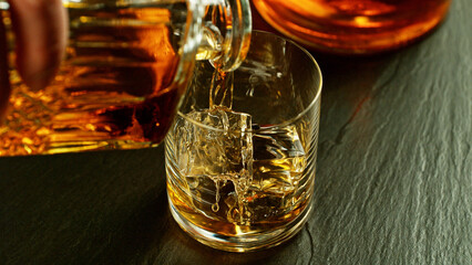 Detail of pouring whiskey into glass with ice cubes.