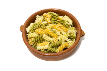 Spiral pasta of three colors, served in a clay bowl. Isolated on a white background.