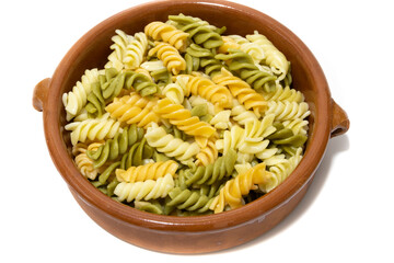 Spiral pasta of three colors, served in a clay bowl. Isolated on a white background.