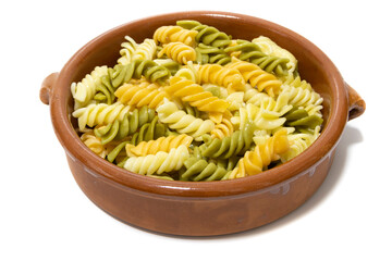 Spiral pasta of three colors, served in a clay bowl. Isolated on a white background.