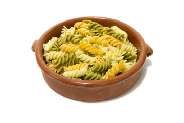 Spiral pasta of three colors, served in a clay bowl. Isolated on a white background.