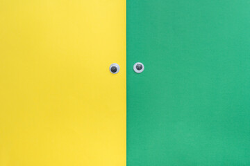 Googly eyes on a yellow and green background with copy space