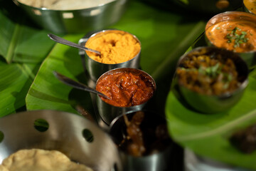 An assortment of traditional Indian seasonings — curry chilis; pickles; and 'gunpowder' splice blend ('milagai podi') — against a backdrop of banana leaves, suggesting southern Indian cuisine.
