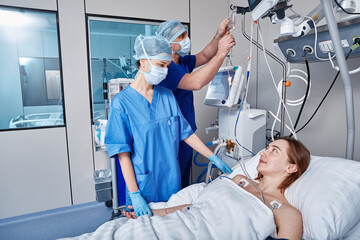 Intensive care patient. Nurses attending to female patient in intensive care unit of hospital - obrazy, fototapety, plakaty