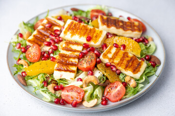 Warm salad with fried halloumi cheese, nuts (cashews and almonds), cherry tomatoes, pomegranate, orange and arugula. Traditional cheese of the Eastern Mediterranean. Selective focus, close-up.