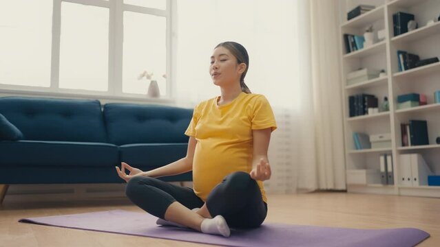 Happy pregnant woman meditating on fitness mat at home, practicing yoga