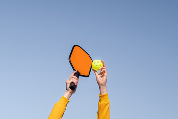 pickleball game, hands over blue sky hitting pickleball yellow ball with paddle, outdoor sport...