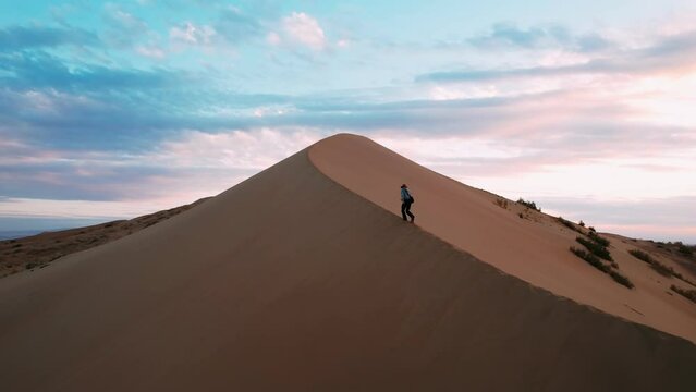 Hiker climb up to the sand dune in the desert. Travel man lost in the desert in africa. Tourist walks out across a sand dune. Desert explorer. Concept: adventure, freedom, exploration, journey. High