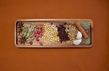 indian spices on a wooden plate on an orange background, top view