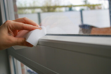 close up of a woman's hand cleaning a window with a white sponge 