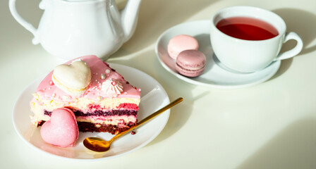 Pink cake with heart shaped macaroons , red tea, white kettle and gold spoon on a black background. Natural light, sunny day