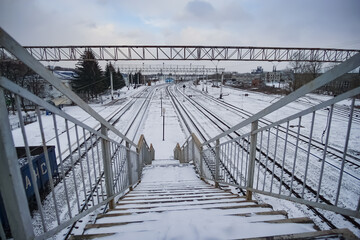 Railway station with a bridge and a train with wagons in winter, railroad tracks on a cloudy day