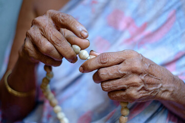 Elderly hindu religious indian woman praying to God using a rosary beads