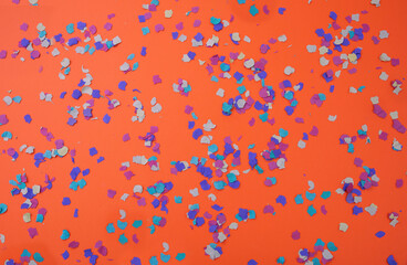 Confetti colorful scattered on orange background. Carnival party, invitation card. Overhead view.