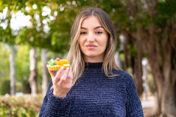 Young pretty Romanian woman holding a tartlet at outdoors with sad expression