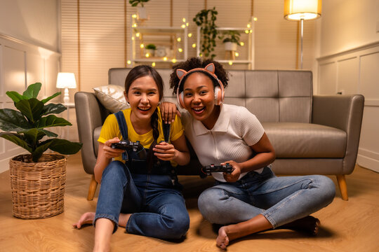 Young  asian and african woman playing video games at home living room at night.Lesbian couples or lgbt activities on vacation inside the room.